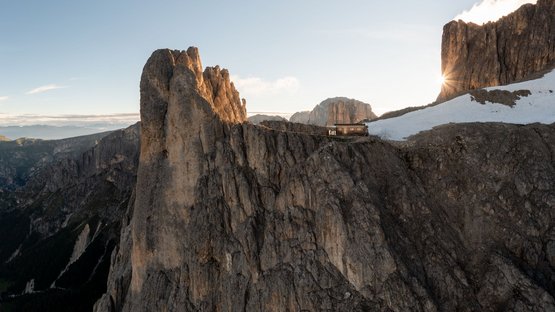 Hotel a Tires al Catinaccio Alba dietro rocce e baita in montagna con neve sulle pendici