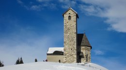 Ihre Hotels in Meran in Südtirol: Hotels im Meraner Land Steinerne Kirche auf schneebedecktem Hügel unter blauem Himmel
