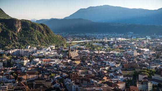 Ihre Hotels in Leifers, der jüngsten Stadt Südtirols Panoramablick auf eine Stadt mit Bergen im Hintergrund bei Sonnenuntergang