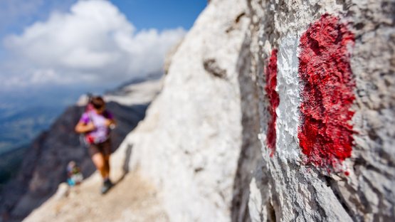 Pala delle Guide (2.890 m) S-Wand »Gino Bellumat« VII (eKN VII–) Wanderwegmarkierung auf Felsen mit verschwommenen Bergsteigern im Hintergrund