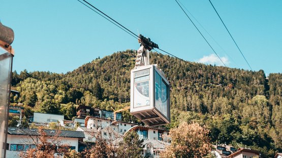 Hotel a Rio di Pusteria in Alto Adige Funivia sopra case con montagna boscosa e cielo blu sullo sfondo