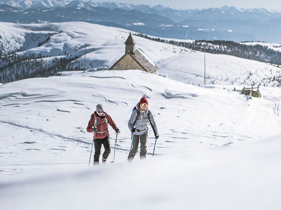 Ihre Hotels in Meran in Südtirol: Hotels im Meraner Land Zwei Wanderer mit Stöcken laufen durch schneebedeckte Berge bei sonnigem Wetter