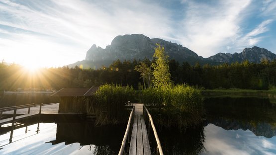 Il Lago di Fiè: uno dei laghi alpini più belli dell’Alto Adige Tramonto su un lago con passerella e montagne sullo sfondo
