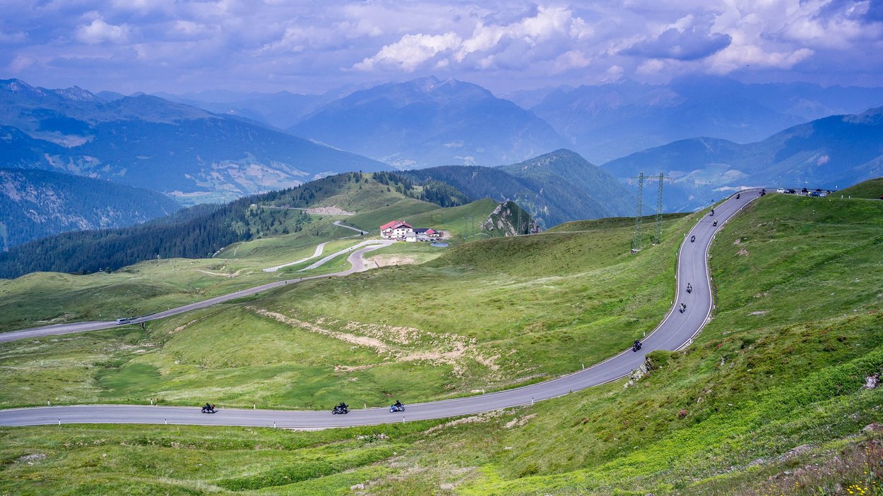 Der Jaufenpass Gebirgsstraße mit Motorrädern und grünen Hügeln unter bewölktem Himmel