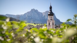 Hotel sulle Dolomiti Campanile con orologio davanti a paesaggio montano e prati verdi in Alto Adige