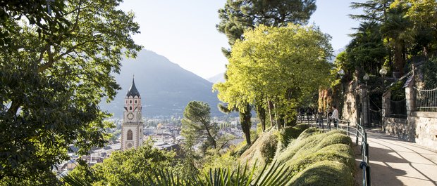 Hotel in Alto Adige 😎☀️ Per vacanze indimenticabili Sentiero con vista su torre della chiesa e città tra alberi verdi e montagne