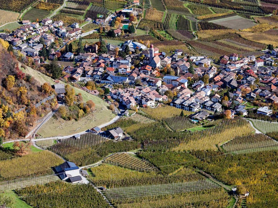 Der Sonnenberg in Naturns Luftaufnahme eines Dorfes umgeben von landwirtschaftlichen Feldern im Herbst
