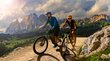 MTB in Alto Adige: la vostra vacanza in bici Due ciclisti su sentiero di montagna con Dolomiti e cielo nuvoloso sullo sfondo