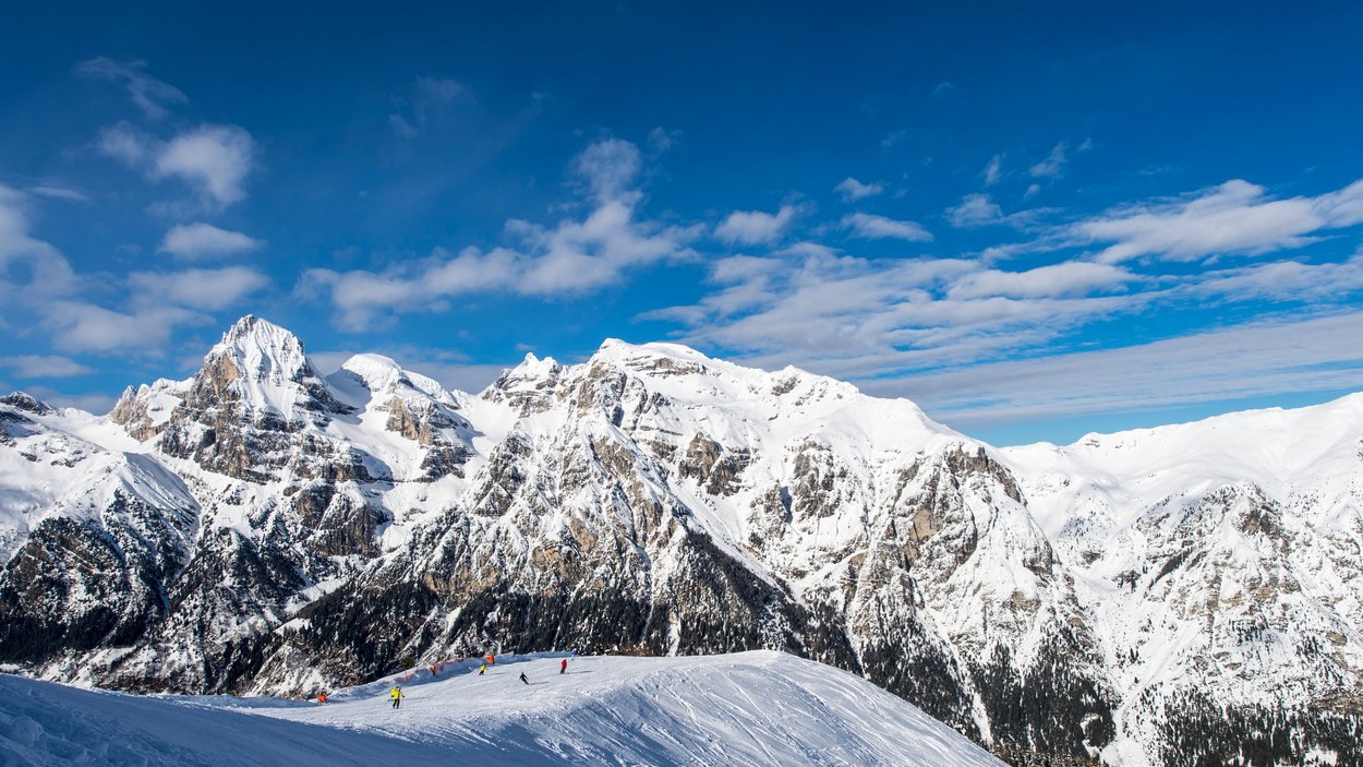 Il vostro paradiso per famiglie Sciatori su montagna innevata con cielo blu e Alpi sullo sfondo