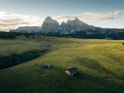 Panorama da sogno dal Rifugio delle Odle Prato verde con piccole baite davanti a montagne rocciose sotto cielo nuvoloso