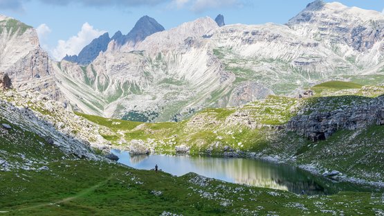 L’acqua turchese del Lago di Crespeina Lago di montagna con prati verdi e vette rocciose, persone sulla riva