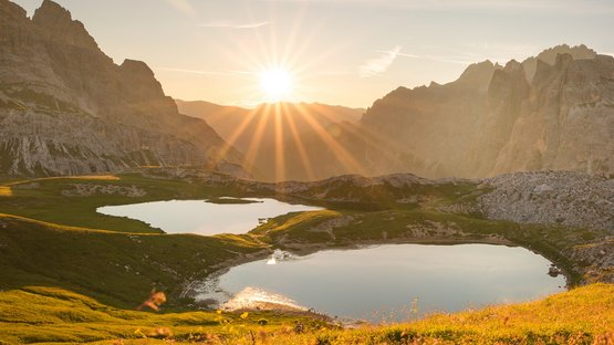Wandern in den Sextner Dolomiten Sonnenuntergang über zwei Bergseen und blühender Wiese in den Alpen