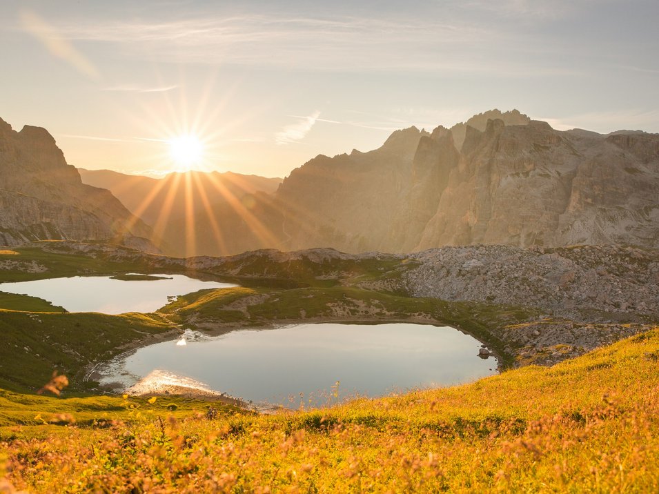 Ihre Hotels in Sexten: traumhafter Urlaub garantiert! Sonnenuntergang über zwei Bergseen und blühender Wiese in den Alpen