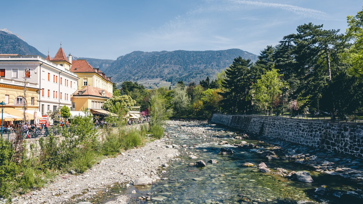 Stadt Centrum – shopping a Merano Fiume con acqua limpida, alberi, edifici storici e montagne sullo sfondo
