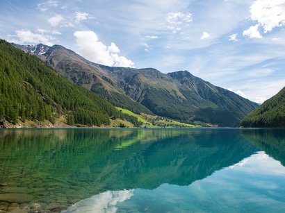 Reschensee: Naturparadies in Südtirol Klarer Bergsee mit Spiegelung der Berge und bewaldeten Hängen unter blauem Himmel