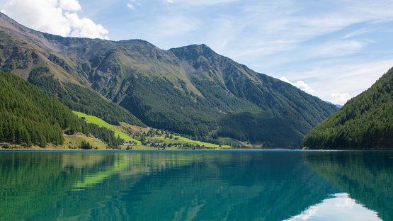 Der Stausee von Vernagt ist ein Paradies für Fischer Klarer Bergsee mit Spiegelung der Berge und bewaldeten Hängen unter blauem Himmel