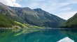 Der Stausee von Vernagt ist ein Paradies für Fischer Klarer Bergsee mit Spiegelung der Berge und bewaldeten Hängen unter blauem Himmel