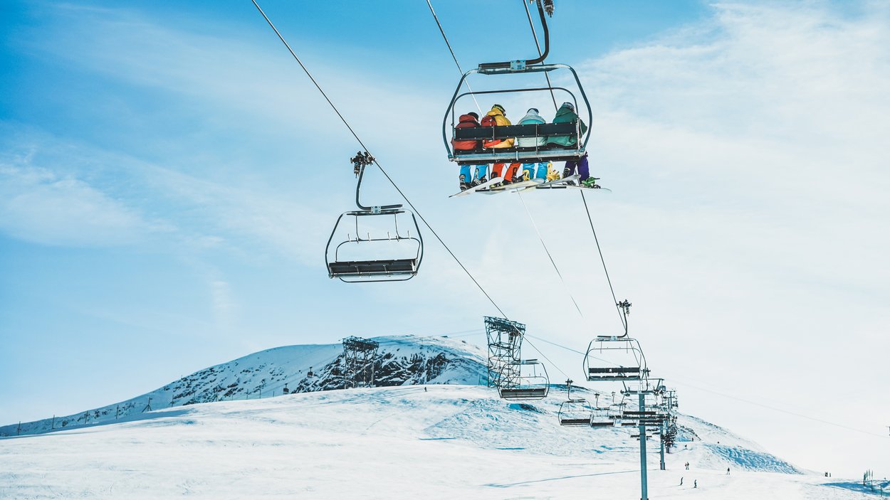 Hotel sulle piste da sci in Trentino-Alto Adige Persone su una seggiovia sopra montagne innevate con cielo sereno