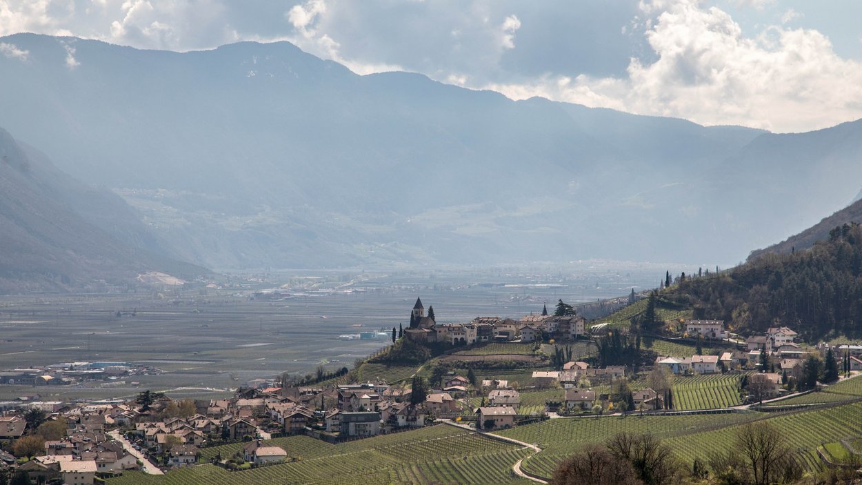 Hotel a Termeno sulla Strada del Vino Paese e vigneti davanti a montagne con cielo nuvoloso