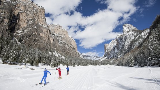 Langlauf in Südtirol: ein absolutes Muss! Langläufer in bunten Anzügen auf verschneiter Berglandschaft mit klar blauem Himmel