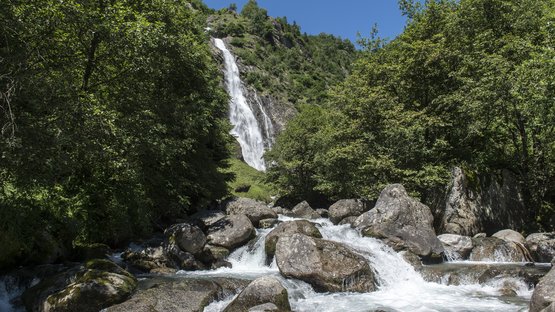 Die eindrucksvollsten Wasserfälle in Südtirol Wasserfall in bewaldetem Gebirge mit Fluss und Felsen im Vordergrund