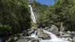Die eindrucksvollsten Wasserfälle in Südtirol Wasserfall in bewaldetem Gebirge mit Fluss und Felsen im Vordergrund