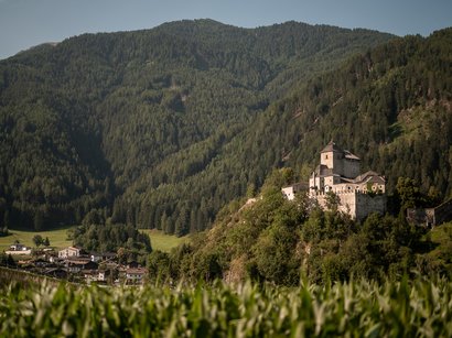 Castel Rodengo Castello su collina boscosa con villaggio in valle sotto cielo azzurro