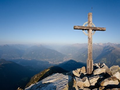 Mit Ausblick auf Meran: die Mutspitze Holzkreuz auf Berggipfel mit Blick auf Tal und Berge unter klarem Himmel