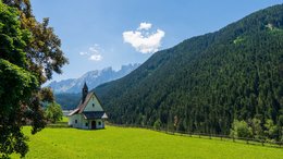 Hotels am Rosengarten und Latemar Kleine Kirche auf grüner Wiese vor bewaldetem Berg und blauem Himmel