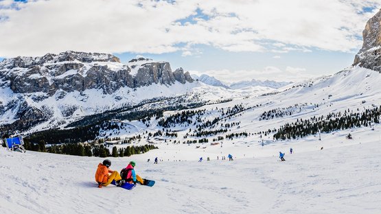 La Sellaronda, per girare attorno al massiccio del Sella Sciatori e snowboarder su pista innevata con rocce e cielo nuvoloso
