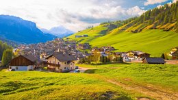 Hotel sulle Dolomiti Villaggio tra verdi colline con montagne sullo sfondo sotto cielo soleggiato