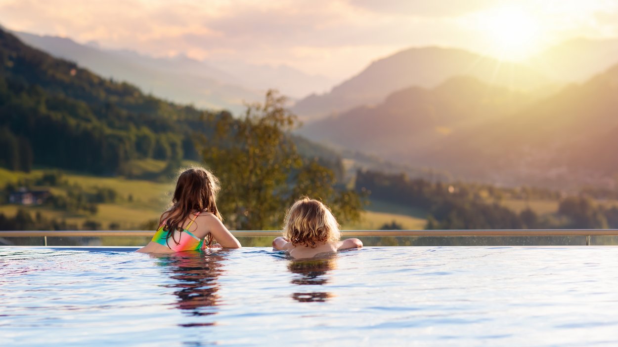 Südtiroler Schwimmbäder Zwei Kinder im Pool mit Blick auf Sonnenuntergang und Berge
