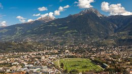 Hotels in St. Martin in Passeier: Ab in den Traumurlaub! Blick auf eine Stadt mit grüner Rennbahn vor Bergen unter blauem Himmel