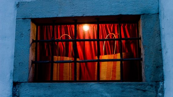 Mercato di Stegona: preparatevi per l’inverno Finestra illuminata con tende rosse e due sedie intrecciate dietro