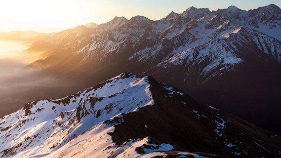 Hotels Vinschgau: Wandern und Skifahren in Südtirol Verschneite Berggipfel bei Sonnenuntergang mit nebligem Tal im Hintergrund