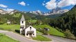 Suchen Sie ein Hotel in Tiers am Südtiroler Rosengarten? Kleine Kirche an einer Straße in grüner alpiner Landschaft mit Bergen im Hintergrund