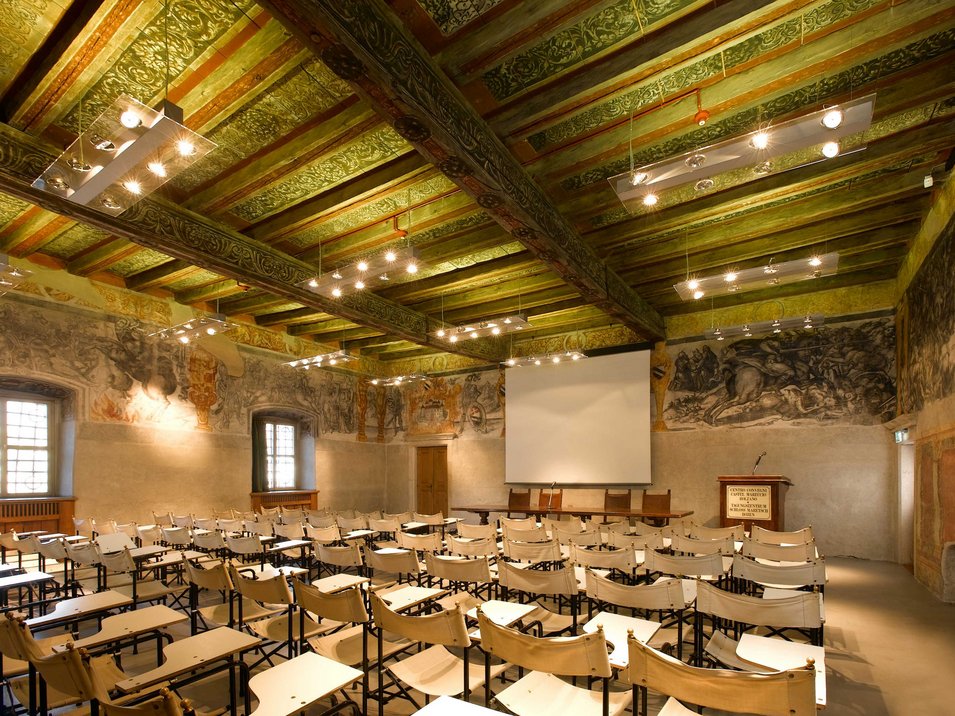 Schloss Maretsch in Bozen Historischer Konferenzraum mit bemalter Holzdecke und Reihen von Stühlen