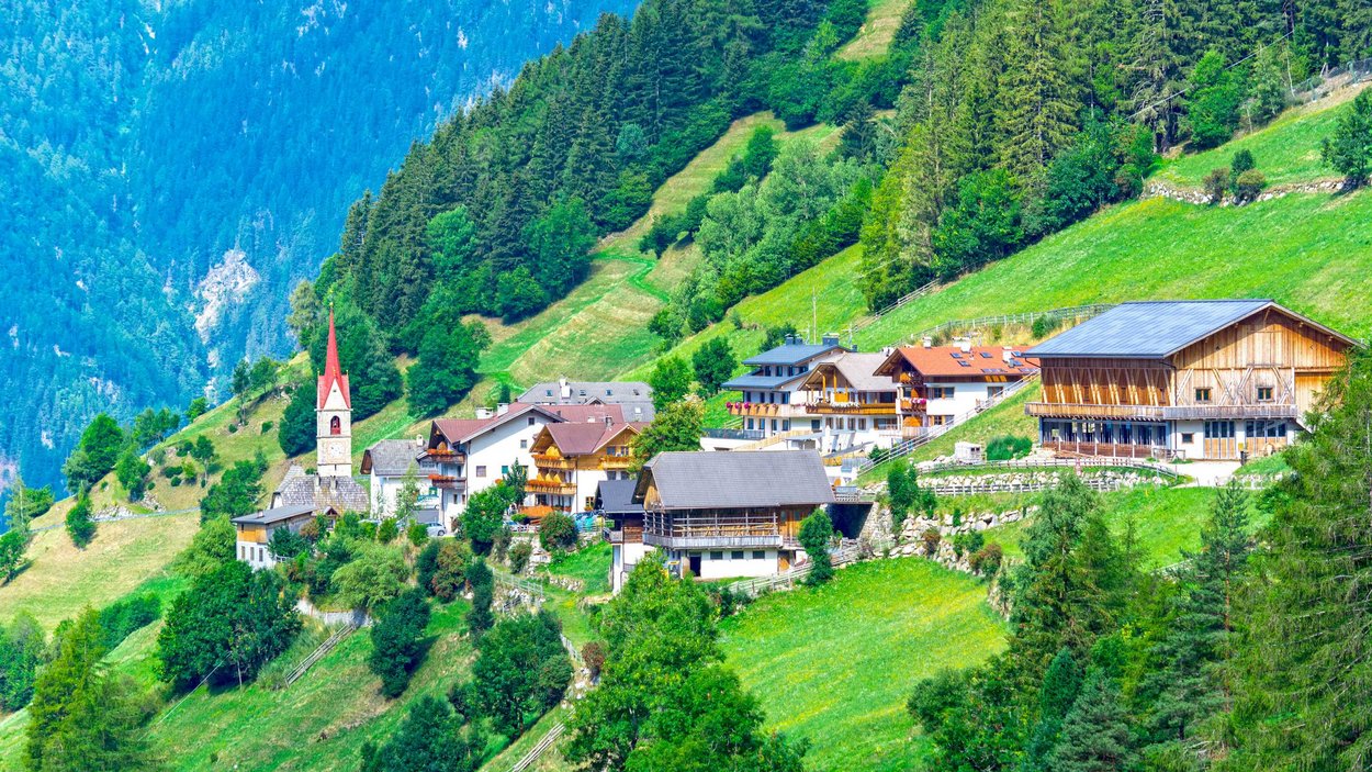 Hotel a Gais in valle Aurina Villaggio con chiesa e case su pendii verdi di montagna sotto cielo blu