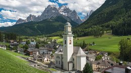 Hotel sulle Dolomiti Veduta di un villaggio con chiesa tra le montagne e le Alpi sullo sfondo