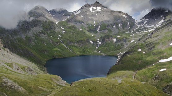 Lago Selvaggio, il più profondo dell’Alto Adige Lago alpino circondato da montagne verdi con neve sotto un cielo nuvoloso
