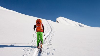 Piz Sesvenna (3204 m.ü.M.) Skifahrer mit rotem Rucksack und grüner Hose beim Aufstieg im Schnee