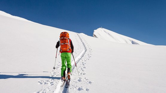 Skitour: Oberbachernspitze Skifahrer mit rotem Rucksack und grüner Hose beim Aufstieg im Schnee