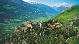 Hotels in St. Martin in Passeier: Ab in den Traumurlaub! Burg auf bewaldetem Hügel mit Tal und schneebedeckten Bergen im Hintergrund