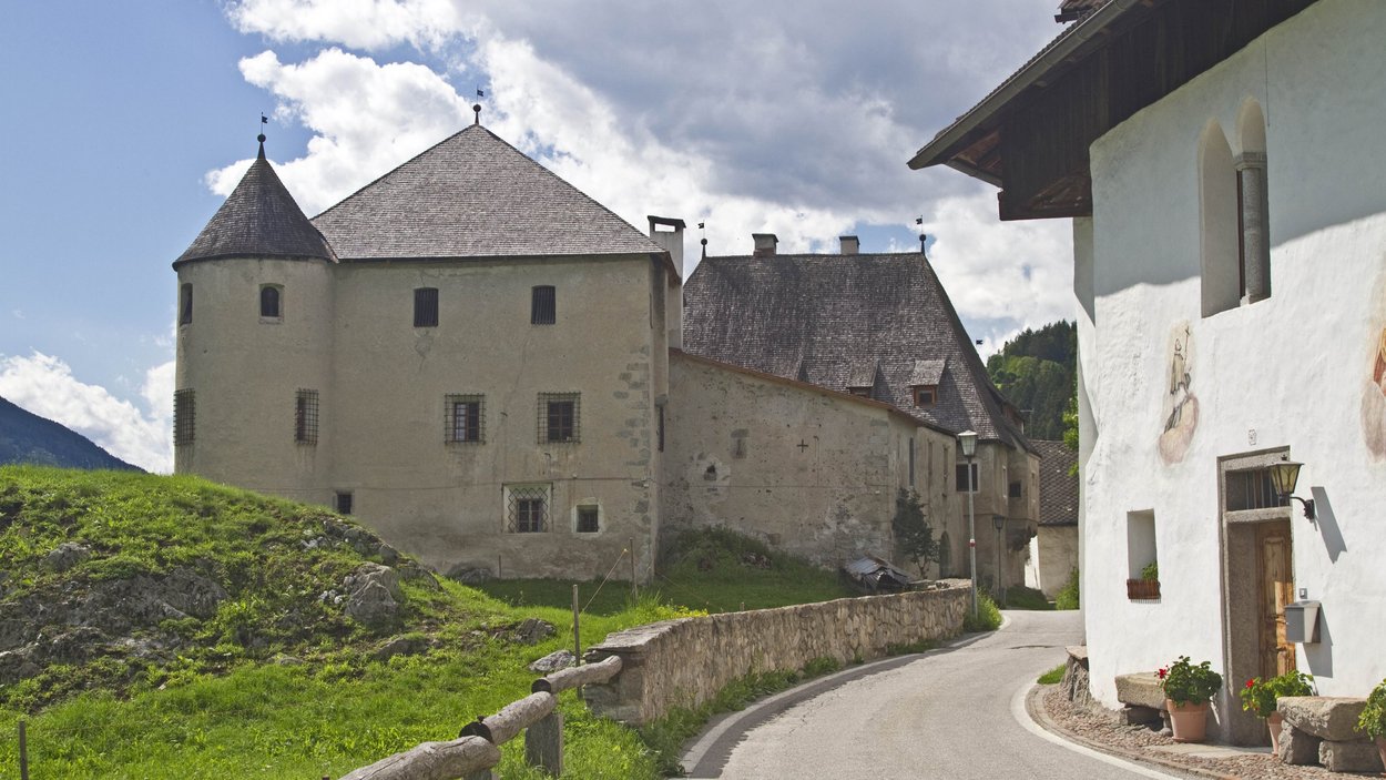 Hotels in St. Lorenzen: willkommen im Pustertal! Historisches Schloss und Dorfstraße mit grünen Wiesen und bewölktem Himmel