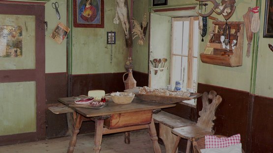 Bauernmuseum Völlan in Südtirol Historische Küche mit Holztisch, Brot, Fleisch und religiösen Symbolen an der Wand