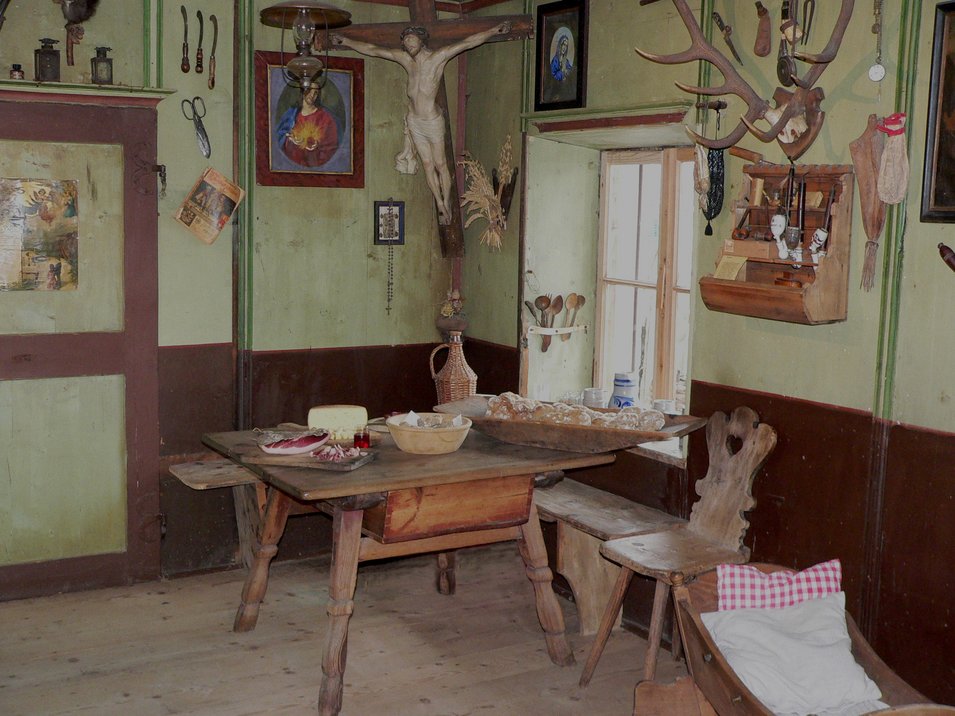 Bauernmuseum Völlan in Südtirol Historische Küche mit Holztisch, Brot, Fleisch und religiösen Symbolen an der Wand