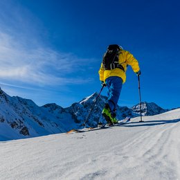 Drei Zinnen-Schneeschuhwanderung Skifahrer in gelber Jacke fährt auf schneebedecktem Berg bei sonnigem Himmel