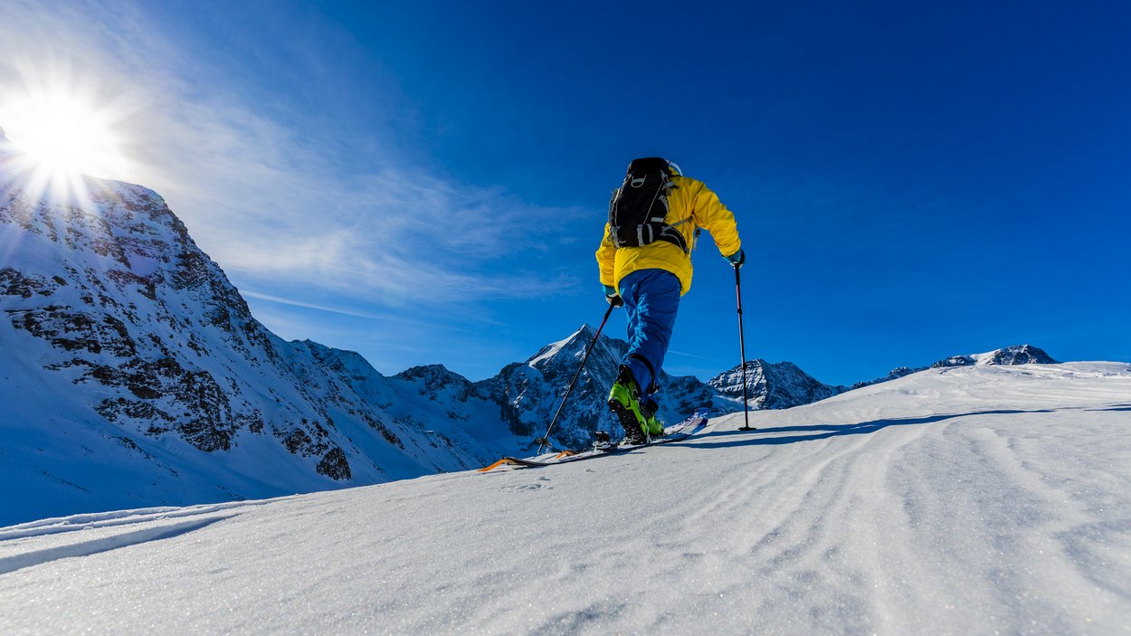Intraprendete spettacolari tour di scialpinismo in Alto Adige! Sciatore con giacca gialla scia su montagna innevata sotto cielo soleggiato