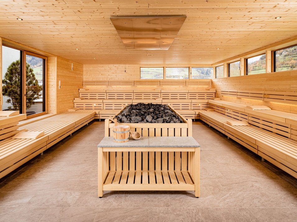 Piscina coperta a Vipiteno Ampia sauna con panche in legno e camino centrale pieno di pietre per sauna