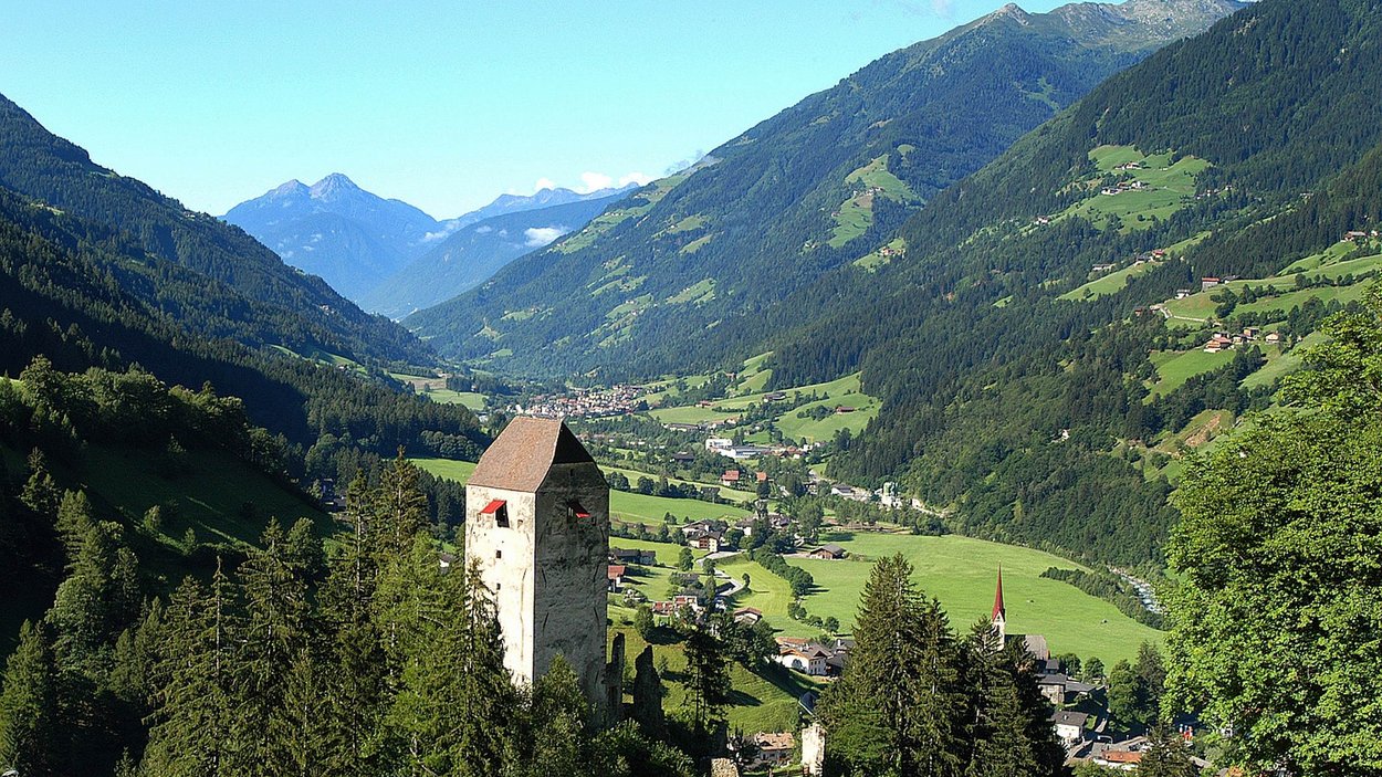 Hotel a San Martino in Passiria Valle di montagna con rovine di castello e prati verdi sotto il cielo azzurro
